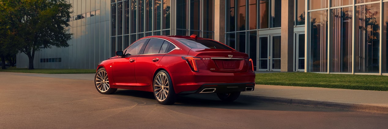 A Driver Side Rear View of a Red 2025 Cadillac Parked Near an Industrial Building