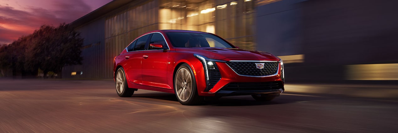 Front View of Red 2025 Cadillac CT5 Driving Past an Industrial Building