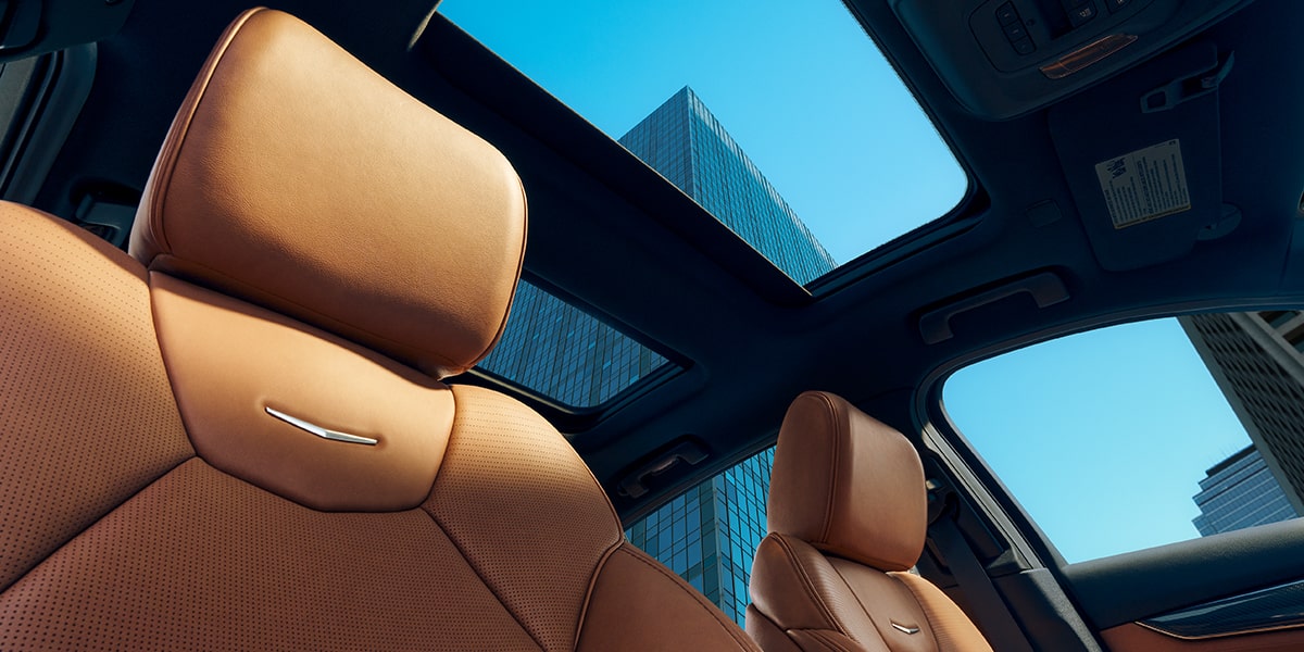 Sol resplandeciente sobre el blasón del Cadillac CT5 2025 en los asientos delanteros de piel y vista del techo corredizo