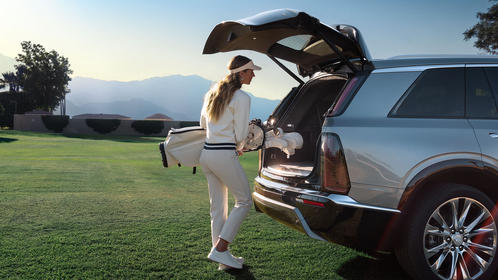A Woman Putting in a Golf Bag Into the Trunk of a Cadillac VISTIQ on a Green Course