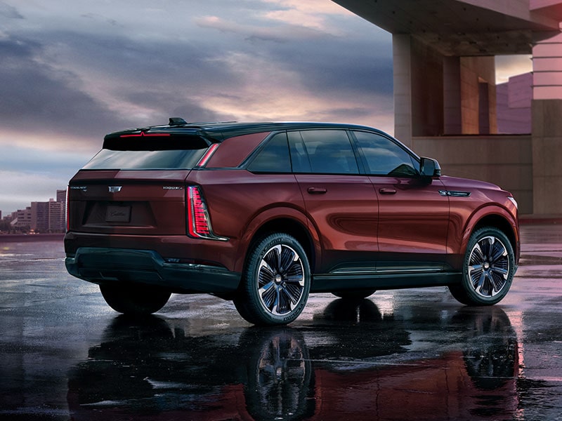 Vista trasera de tres cuartos de una SUV ESCALADE IQ EV 2026 en granate estacionada, bajo su reflejo
