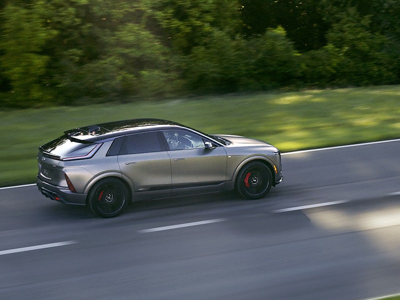 Three-quarter Driver's Side View of a Silver 2026 Cadillac LYRIQ-V Electric SUV Driving Down a Road