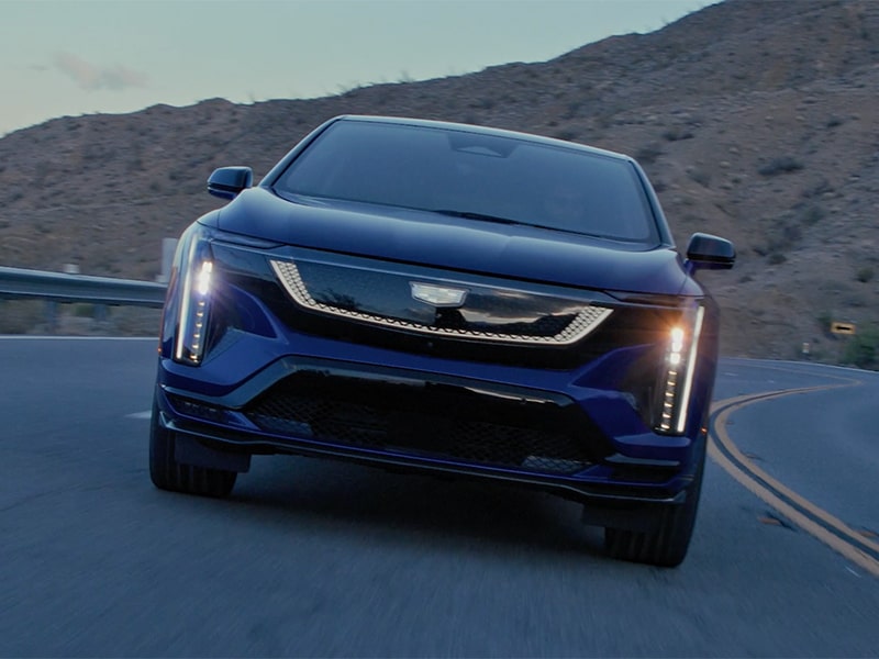 Front View of the 2026 OPTIQ-V Driving Through the Dusk Utilizing its Headlights