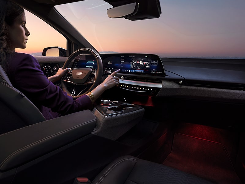 A Woman in the Driver Seat of a 2026 Cadillac OPTIQ Reaching to Press the Infotainment Screen