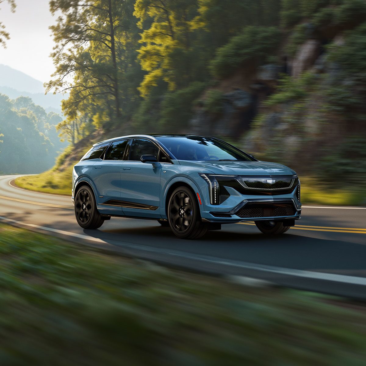 Three-quarters View of a Blue 2026 OPTIQ-V Driving Through a Mountain Road