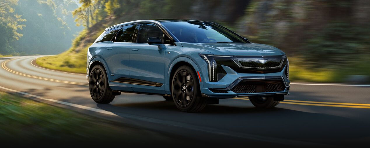 Three-quarters View of a Blue 2026 OPTIQ-V Driving Through a Mountain Road