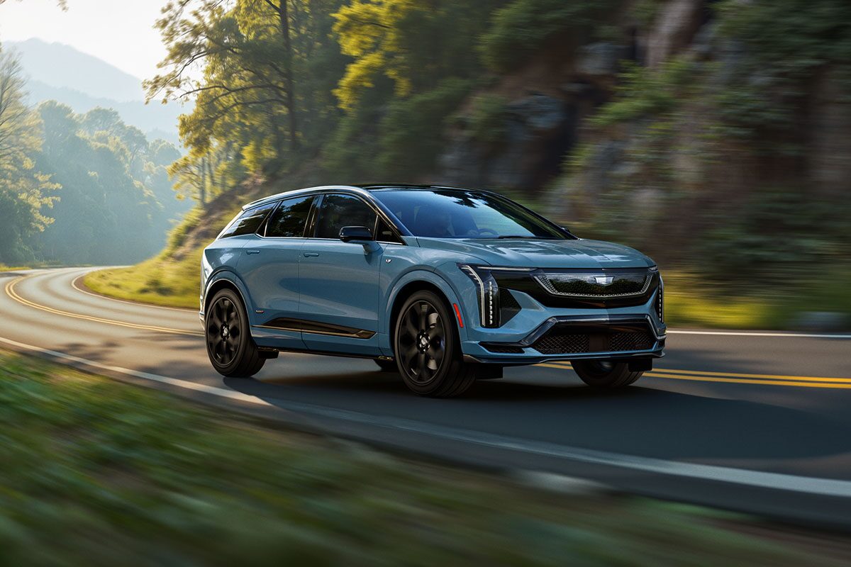 Three-quarters View of a Blue 2026 OPTIQ-V Driving Through a Mountain Road