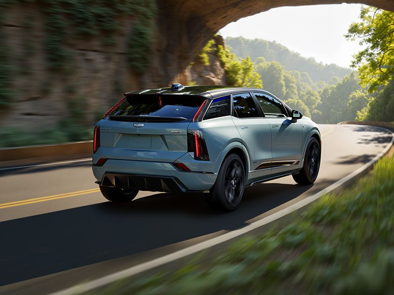 Rear View of a Blue 2026 OPTIQ-V Driving on a Curve of a Mountain Row