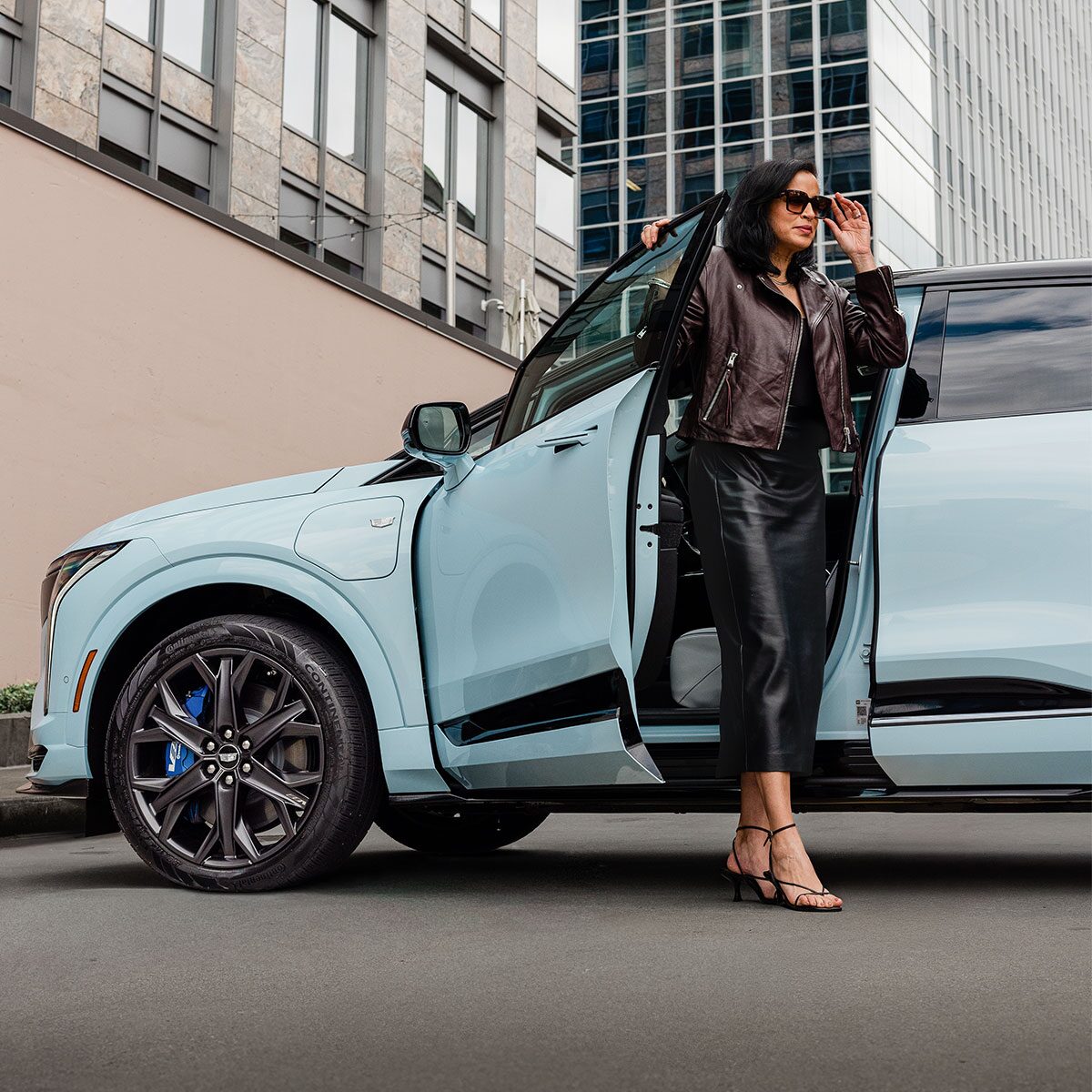 A Man in Sunglasses Standing Next to a Parked Blue 2026 OPTIQ-V