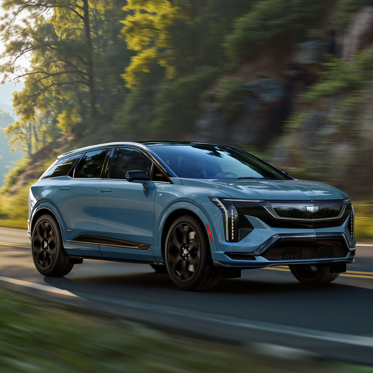 Three-quarters View of a Blue 2026 OPTIQ-V Driving Through a Mountain Road