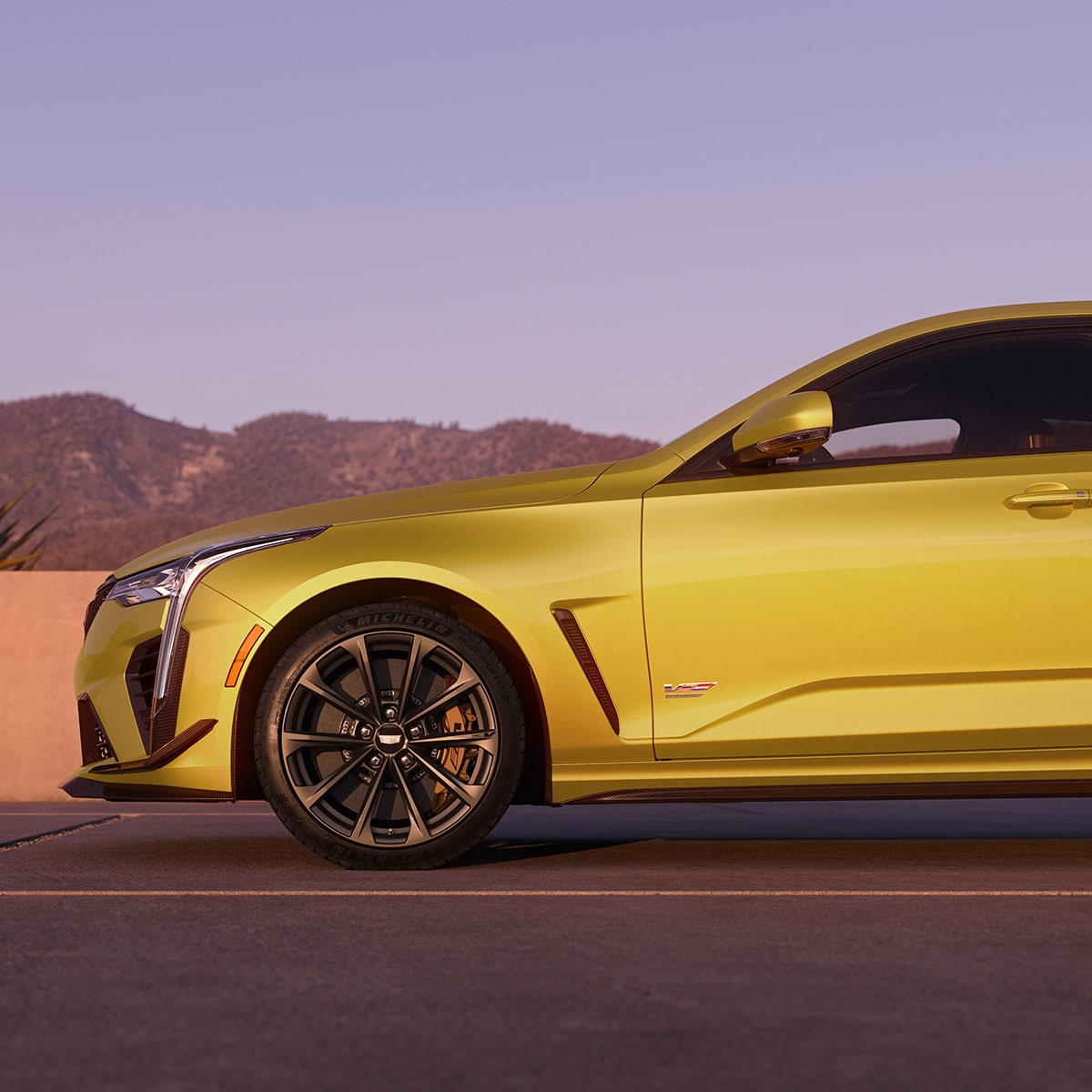 The Front Half Side Profile of a Yellow CT4-V Driving Past Mountains