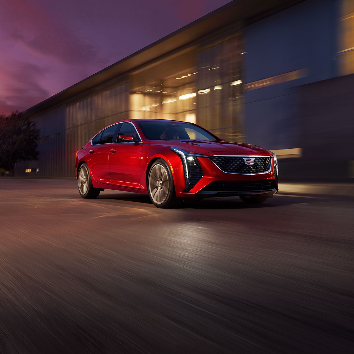 Front View of Red 2026 Cadillac CT5 Driving Past an Industrial Building