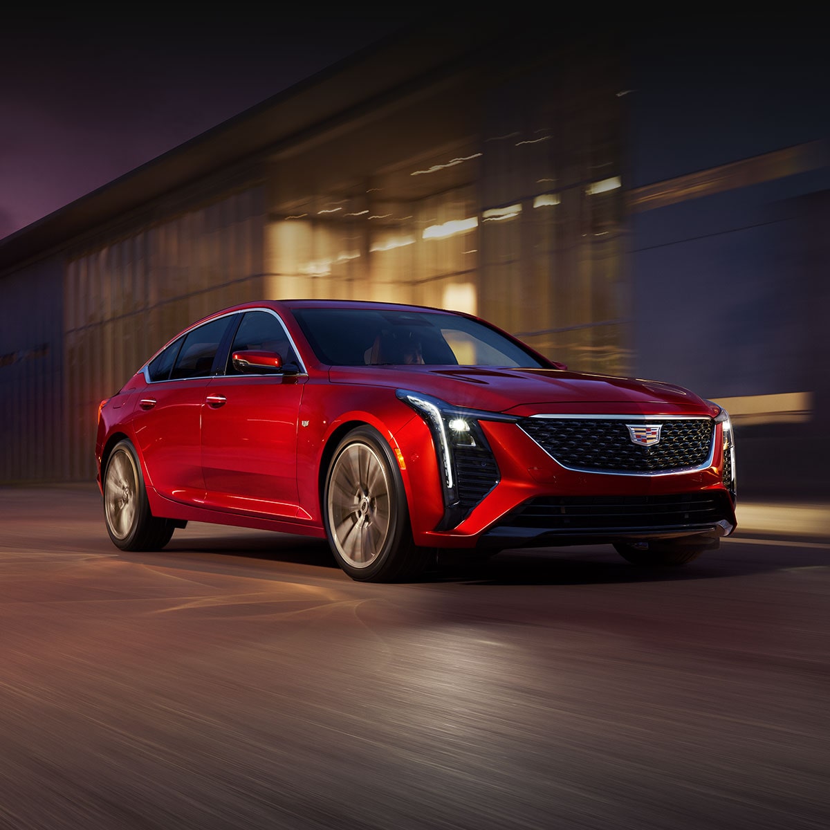  Front View of Red 2026 Cadillac CT5 Driving Past an Industrial Building