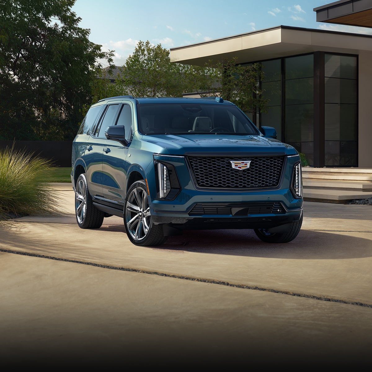 Three-Quarter View of a Blue 2026 Cadillac Escalade Parked in Front of a Modern Home