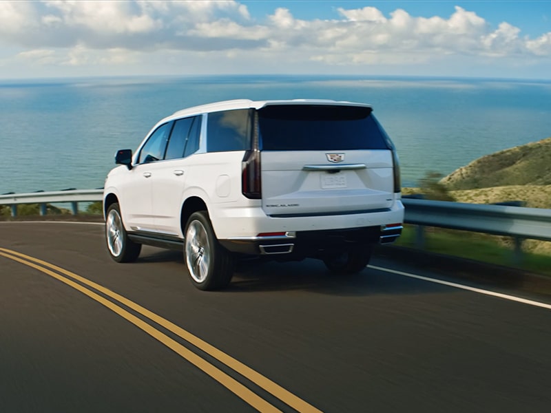 Rear View of a White 2026 Cadillac Escalade Driving Down the Highway Near the Ocean