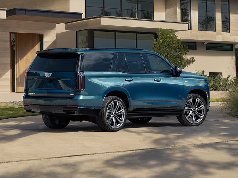 Three-Quarter Rear View of a Blue 2026 Cadillac Escalade Parked in Front of a Modern Home