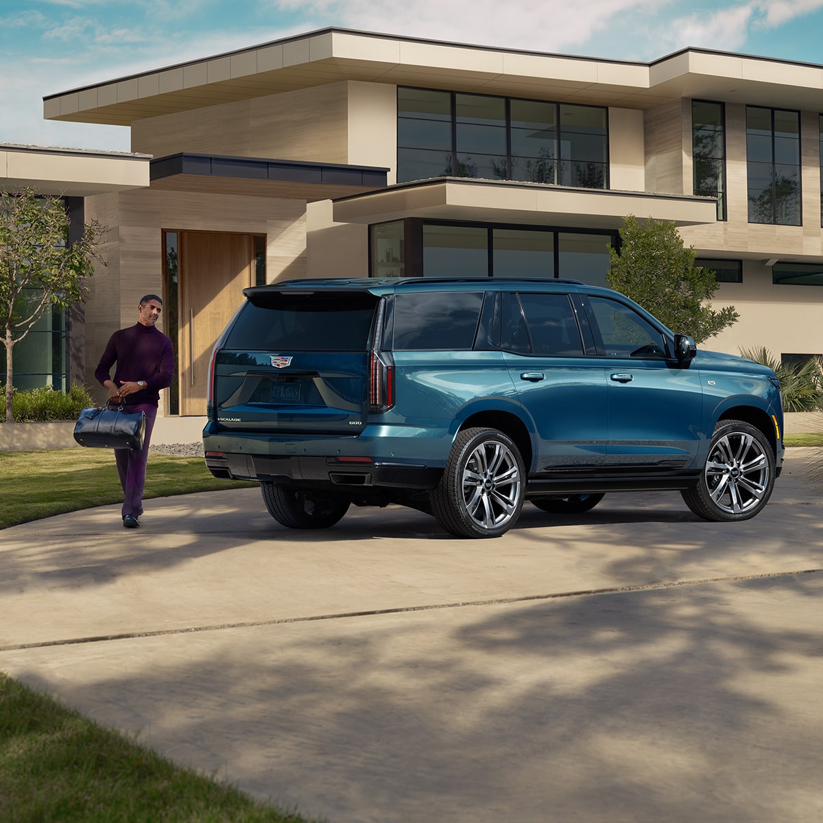 A Man Walking with Luggage to a Blue 2026 Cadillac Escalade Parked in Front of a Modern Home