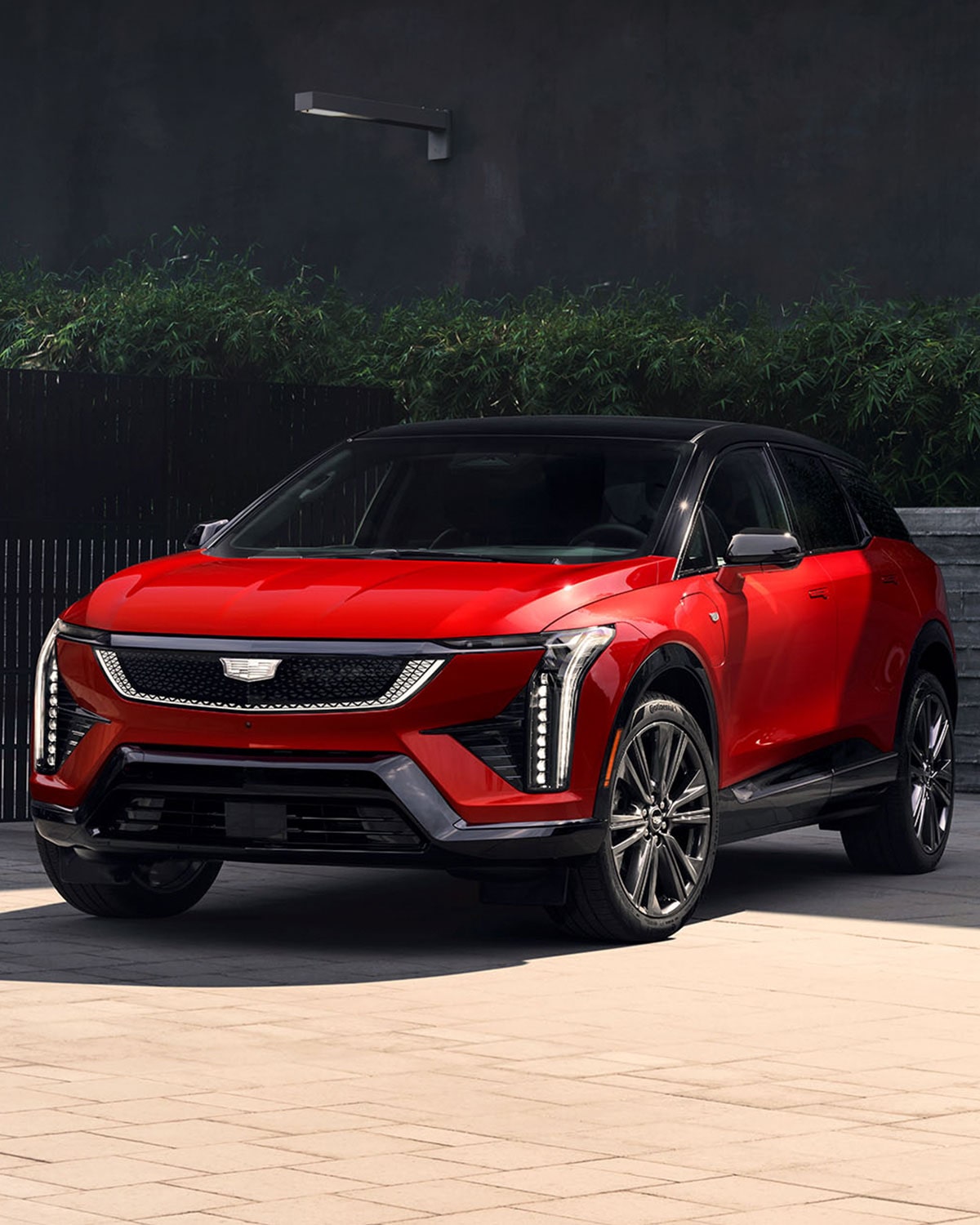 Three-quarter View of a Red Cadillac OPTIQ Parked by a Brick Wall and Green Shrub