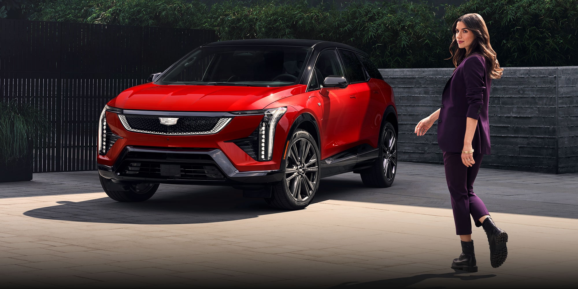 A Fashionably Dressed Woman Walking Towards a Parked Red Cadillac OPTIQ