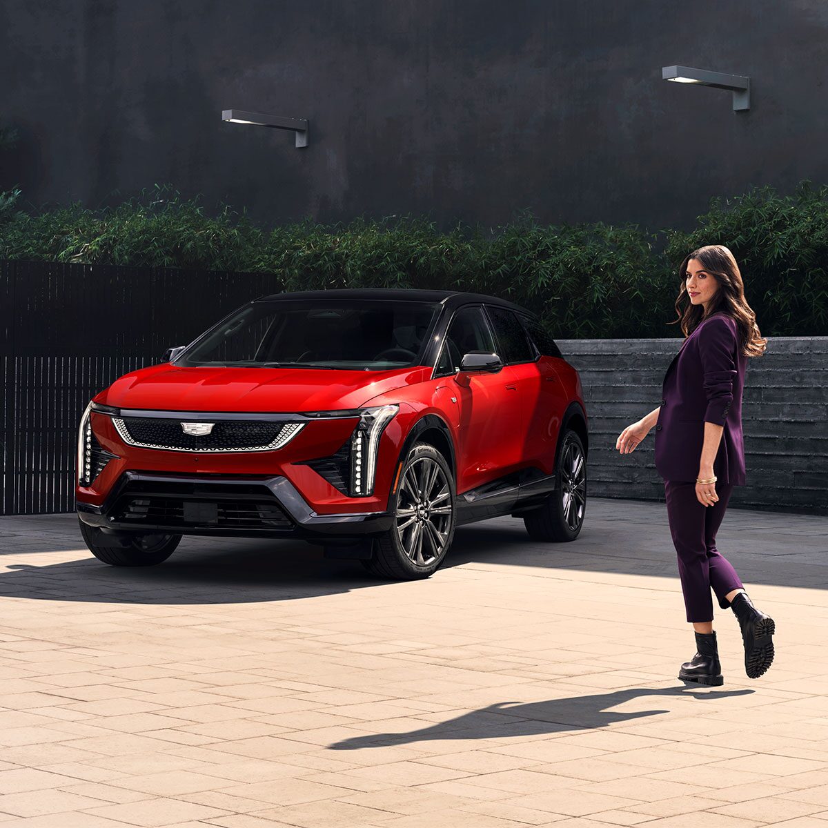 A Fashionably Dressed Woman Walking Towards a Parked Red Cadillac OPTIQ