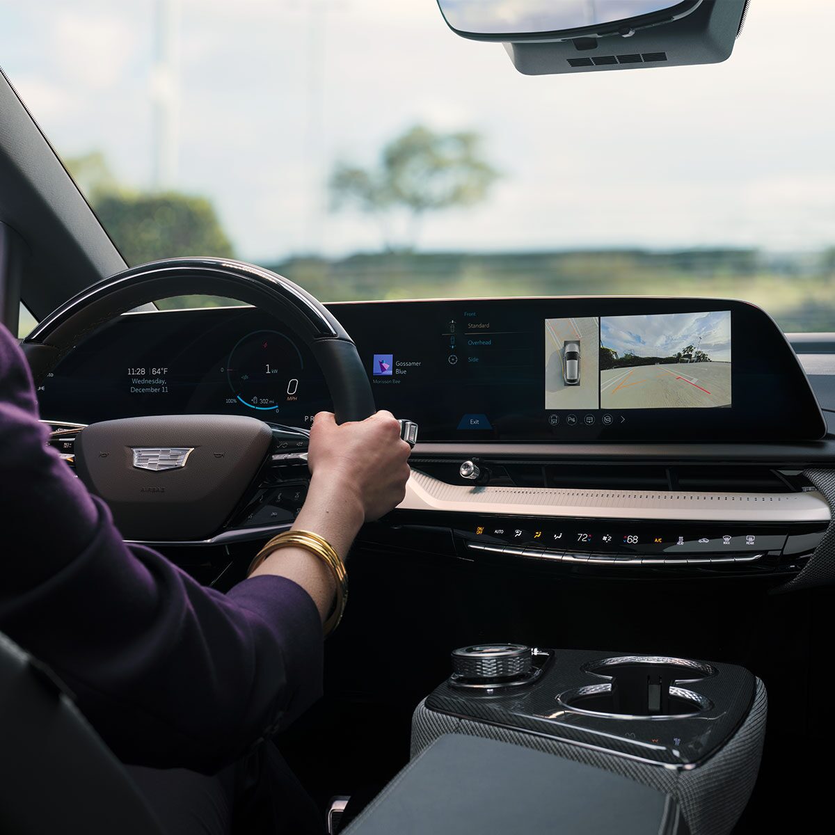 A Woman Holding onto the OPTIQ's Steering Wheel with the Display Screen Showing a Bird's Eye View of the Vehicle Parking