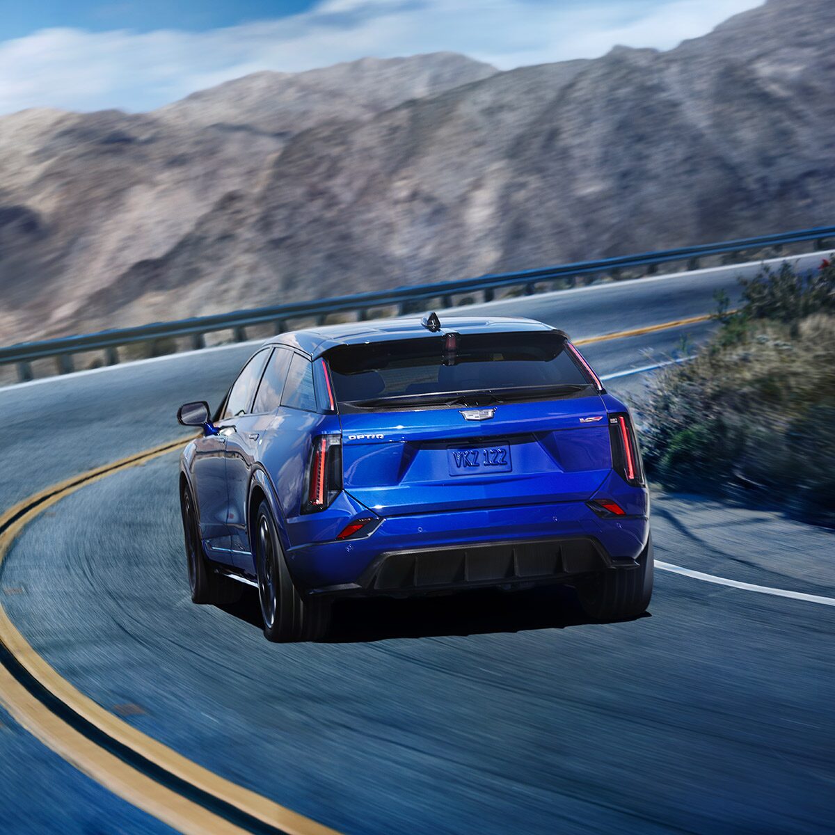 Rear View of a Blue OPTIQ-V Driving on a Curve of a Mountain Road