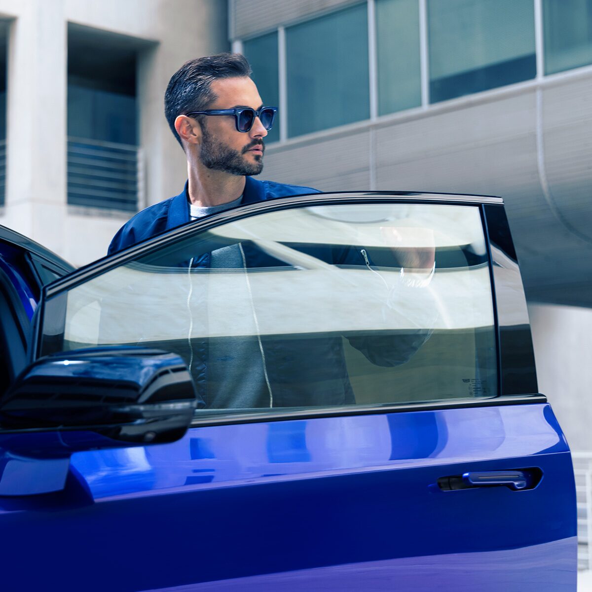 A Man in Sunglasses at the Driver's Seat Door Getting Ready to Get into a Blue OPTIQ-V