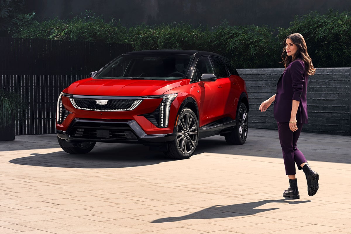 A Fashionably Dressed Woman Walking Towards a Parked Red Cadillac OPTIQ