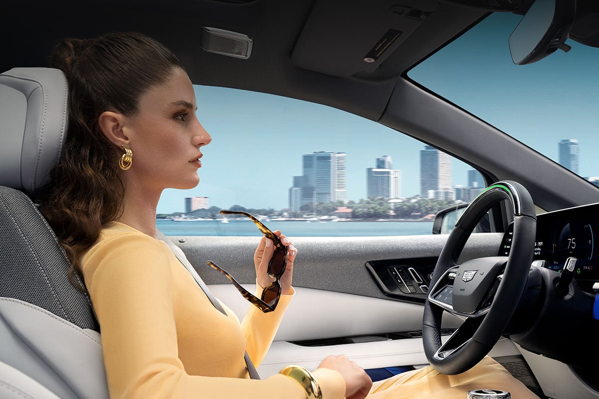 Passenger View of a Woman Driving a Cadillac OPTIQ Past the City While Utilizing Super Cruise Hands-free Technology