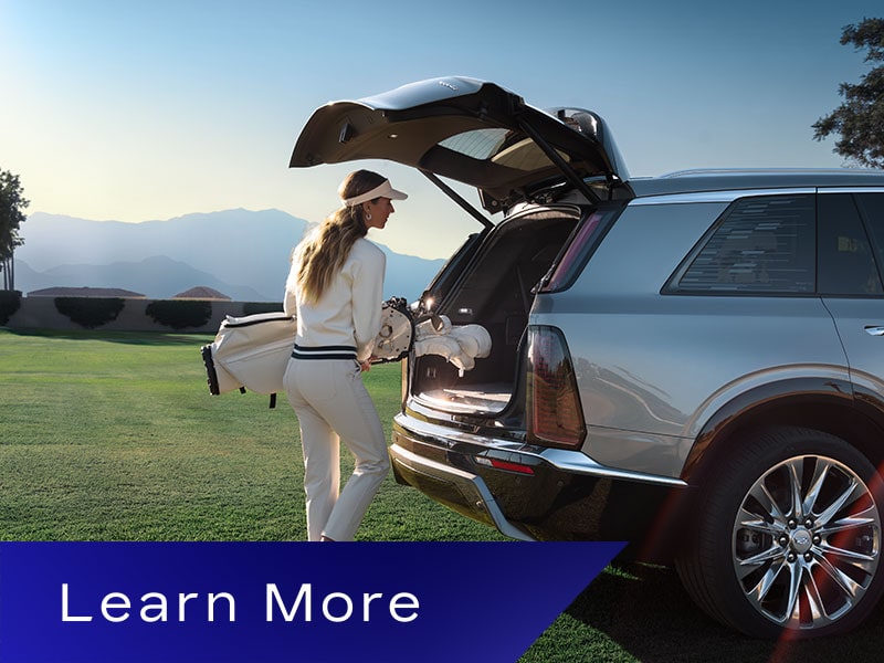 A Woman Putting in a Golf Bag Into the Trunk of a Cadillac VISTIQ on a Green Course