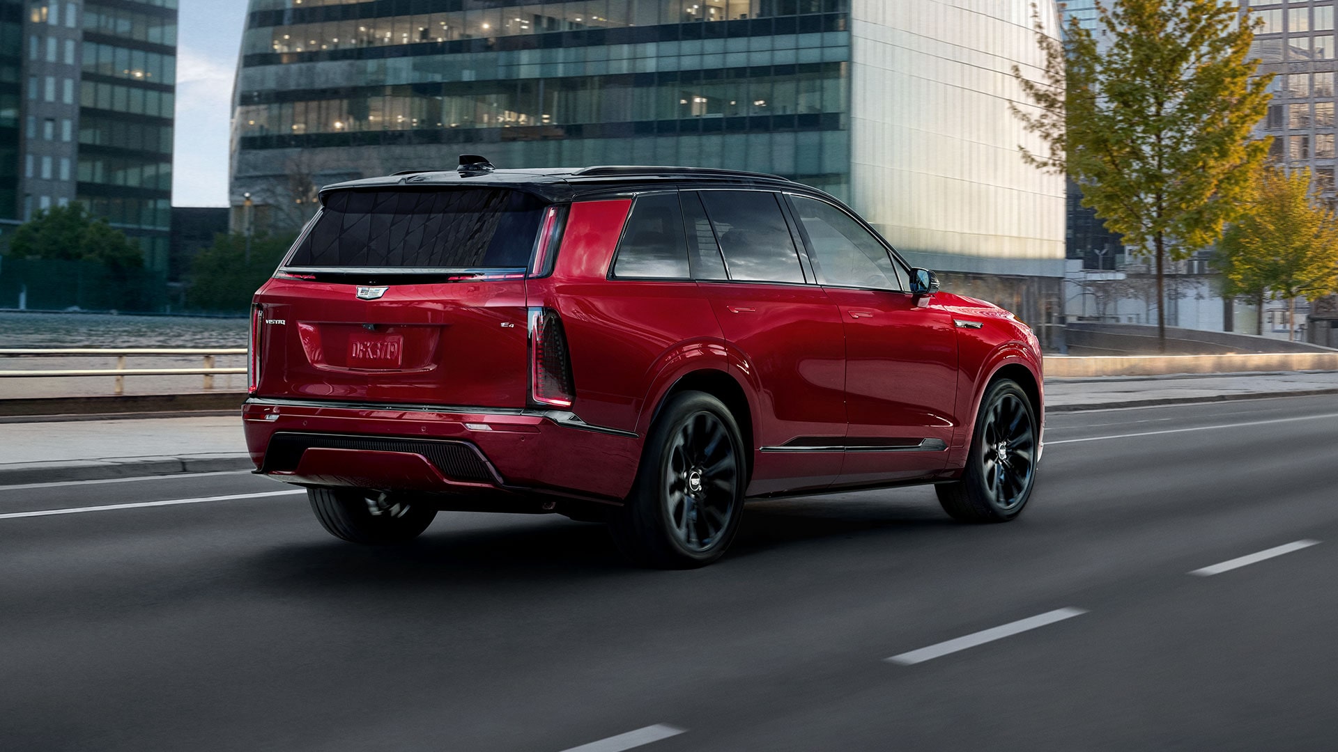 A Rear Three-Quarter View of a Red 2027 Cadillac VISTIQ Driving on a City Street