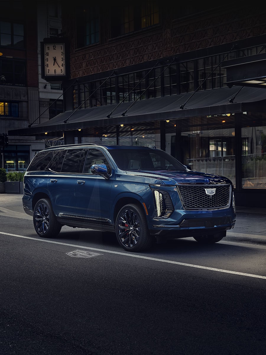 A Blue 2027 Cadillac Escalade Parked on a City Street in Front of Downtown Buildings with Text Overlay Reading "2027 Escalade Features"