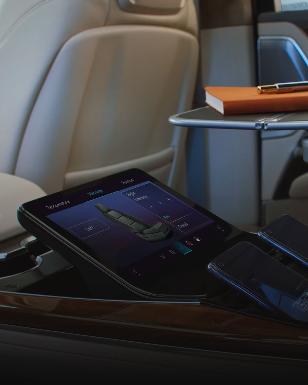 The 2027 Escalade Second Row Command Center Touchscreen Integrated Into the Center Console Next to a Book on the Chair's Pull Out Table