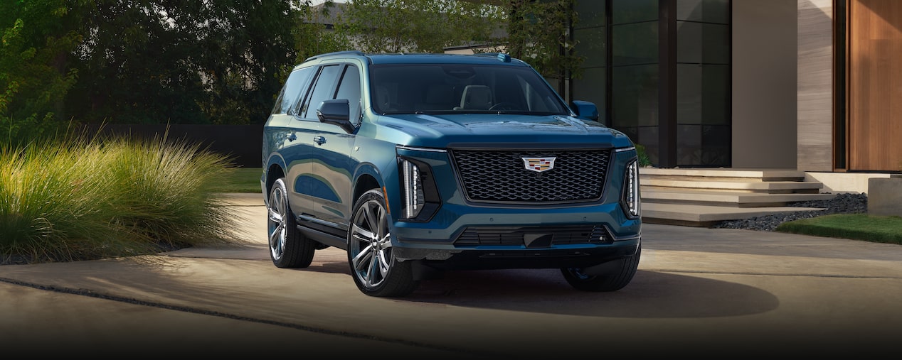 Vista de medio perfil de una Cadillac Escalade 2025 azul estacionada delante de una casa moderna