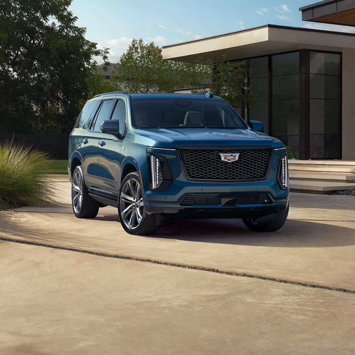 Vista de medio perfil de una Cadillac Escalade 2025 azul estacionada delante de una casa moderna