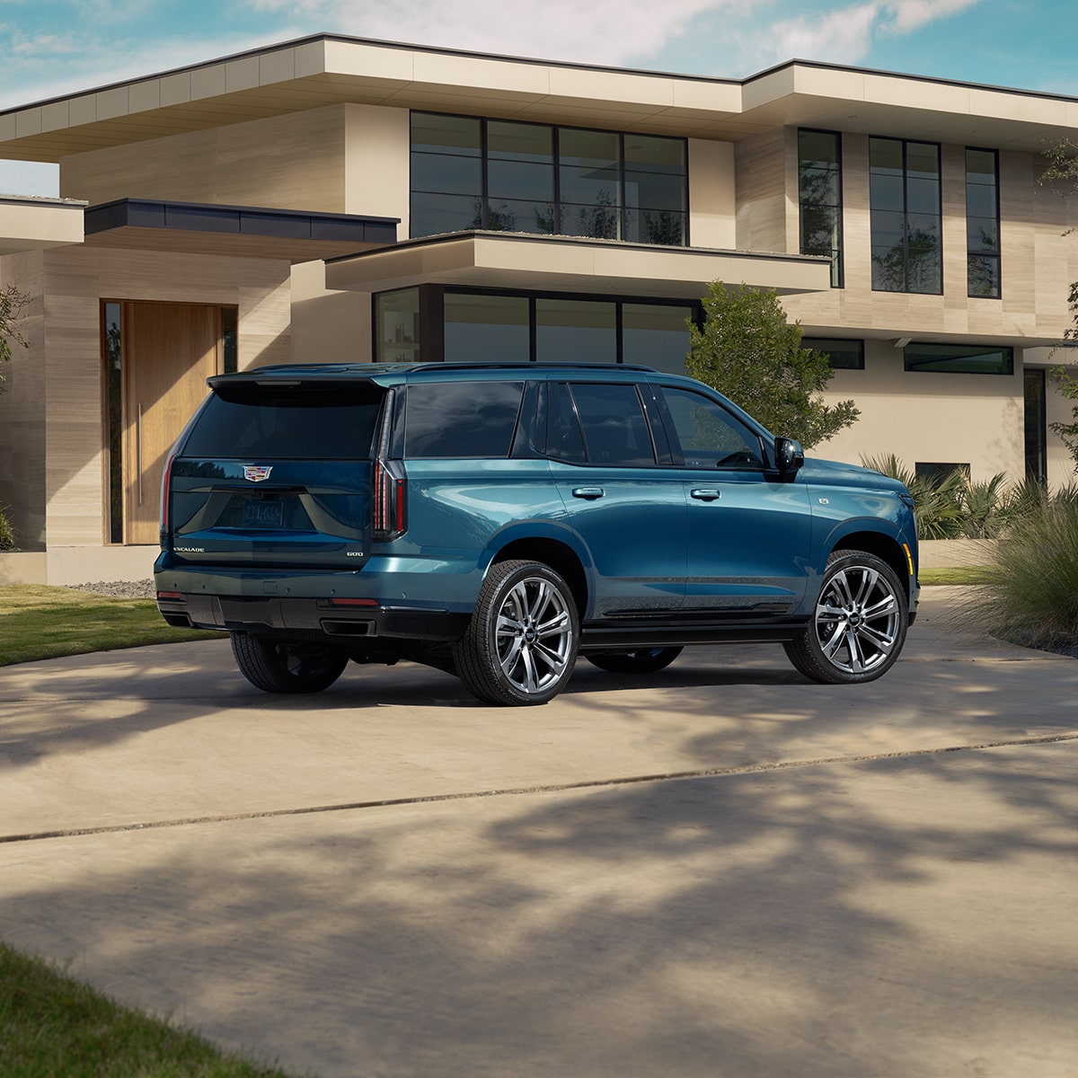 Vista trasera de medio perfil de Cadillac Escalade 2025 azul estacionada delante de una casa moderna