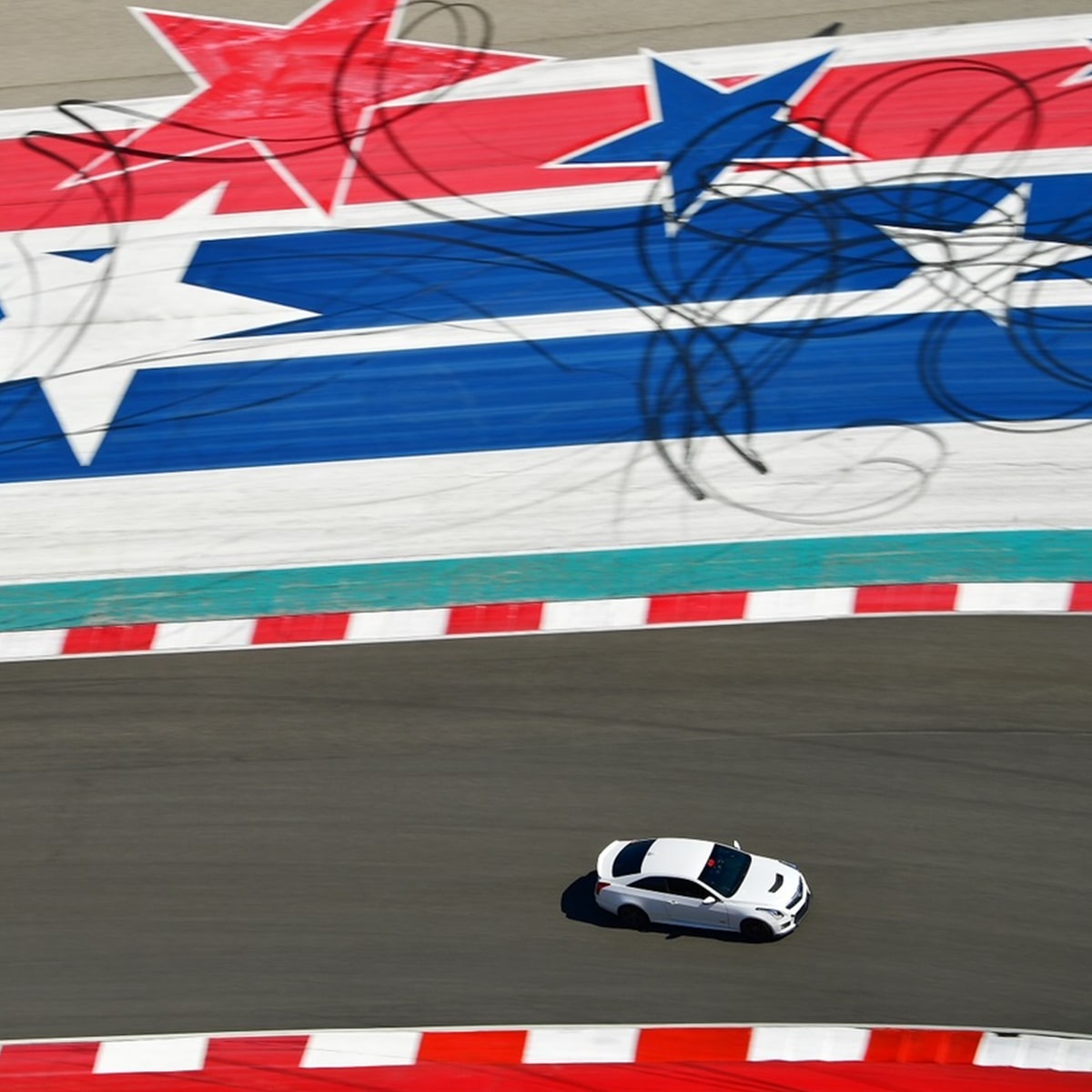 Cadillac V-Series en Blanco en Motor Speedway, con un mural en rojo, blanco y azul en una pared de la pista de carreras