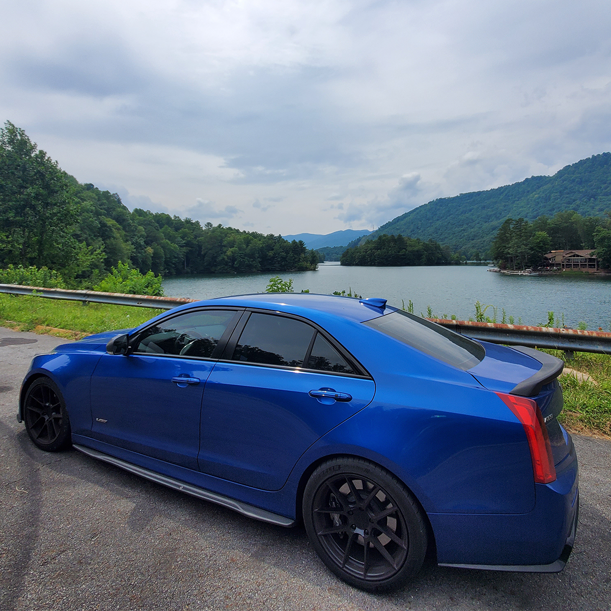 Vista trasera lateral de un Cadillac V-Series en Azul estacionado en frente de un lago y montañas