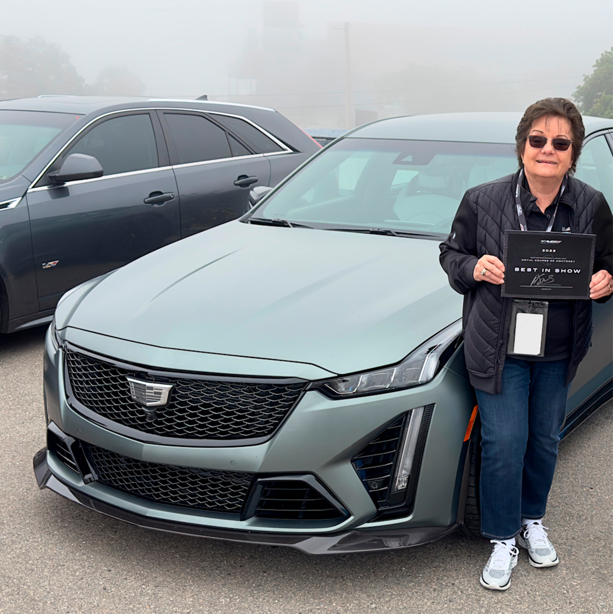 Vista delantera de Cadillac CT5-V Blackwing, con una mujer sosteniendo un premio "Best of Show" de Cadillac