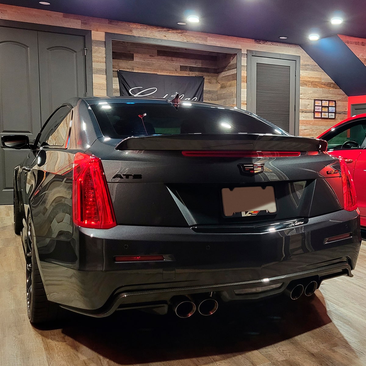 Vista trasera de Cadillac ATS-V en Negro estacionado al lado de un sedán Cadillac en Rojo, en una sala de exposición con paredes de madera y detalles de color negro
