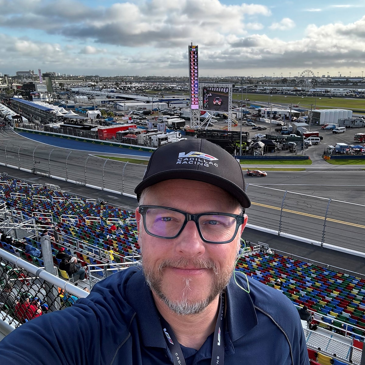 Hombre tomándose una selfie en las gradas de la pista de carreras de Cadillac, con una pista de carreras de fondo