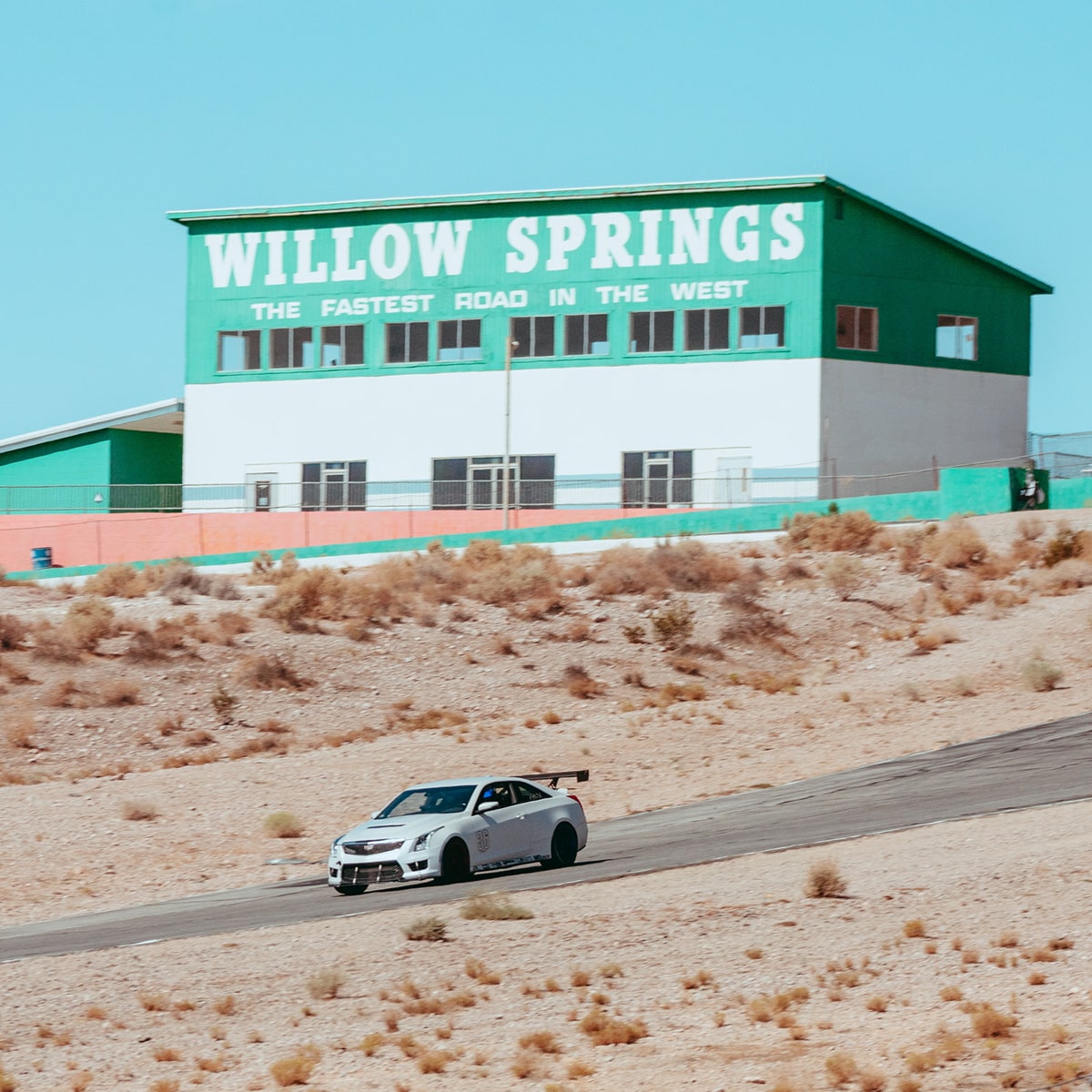 Cadillac V-Series modificado circulando por un camino desérticos, con un almacén de automovilismo de fondo