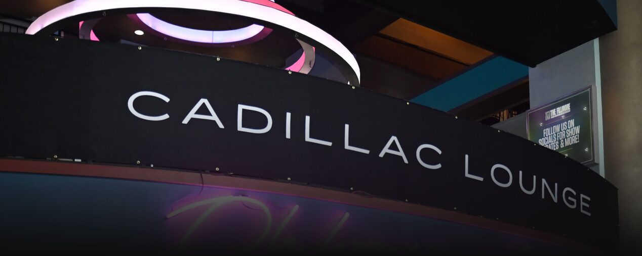 Primer plano de un letrero de salón de Cadillac y un letrero de neón que dice "Oh how sweet it is"