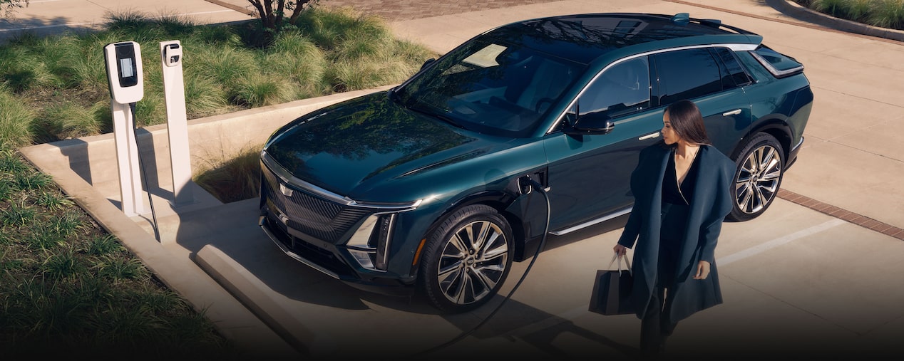 Una mujer de negocios se aleja de un Cadillac LYRIQ que se está cargando en un cargador público