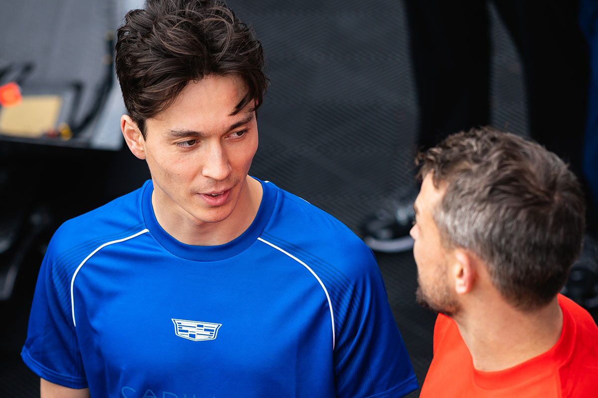 A Person Wearing a Bright Blue Shirt With a Cadillac Logo Talks to Another Person in a Red Shirt Standing Nearby.