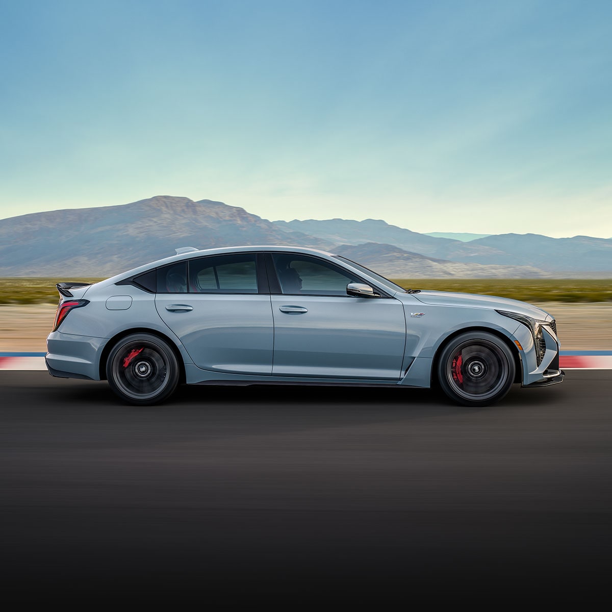 A Silver Cadillac CT5-V Blackwing Driving Down a Road with Fields and Mountains in the Background.