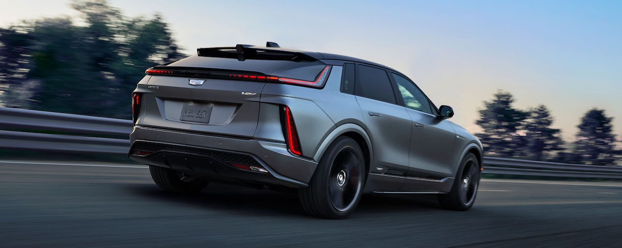 A Rear Angled View of a Cadillac OPTIQ-V Driving Down a Highway with Trees Next to it.