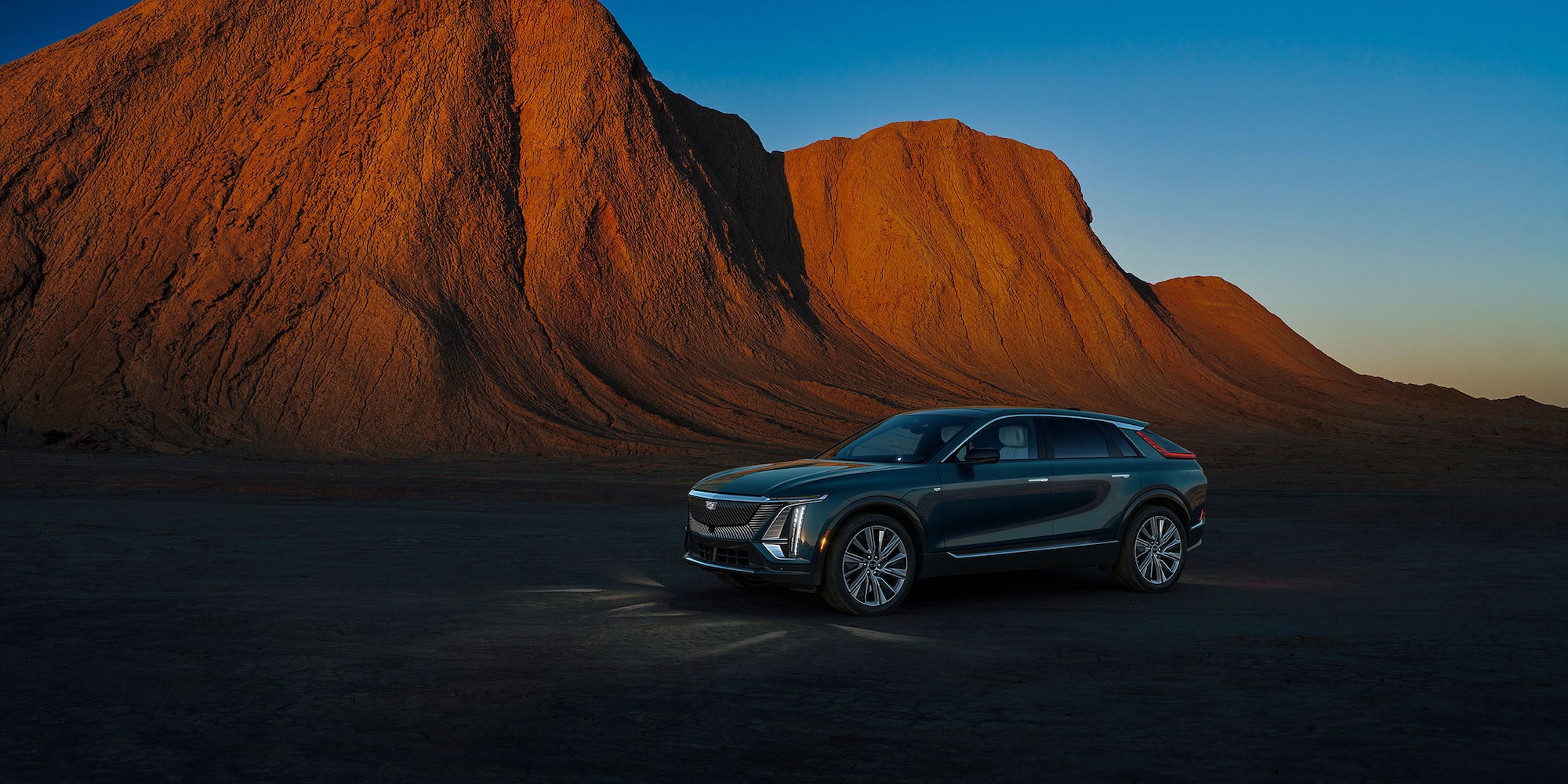  2024 Cadillac LYRIQ Luxury in Emerald Green Metallic parked in desert landscape by mountain. 