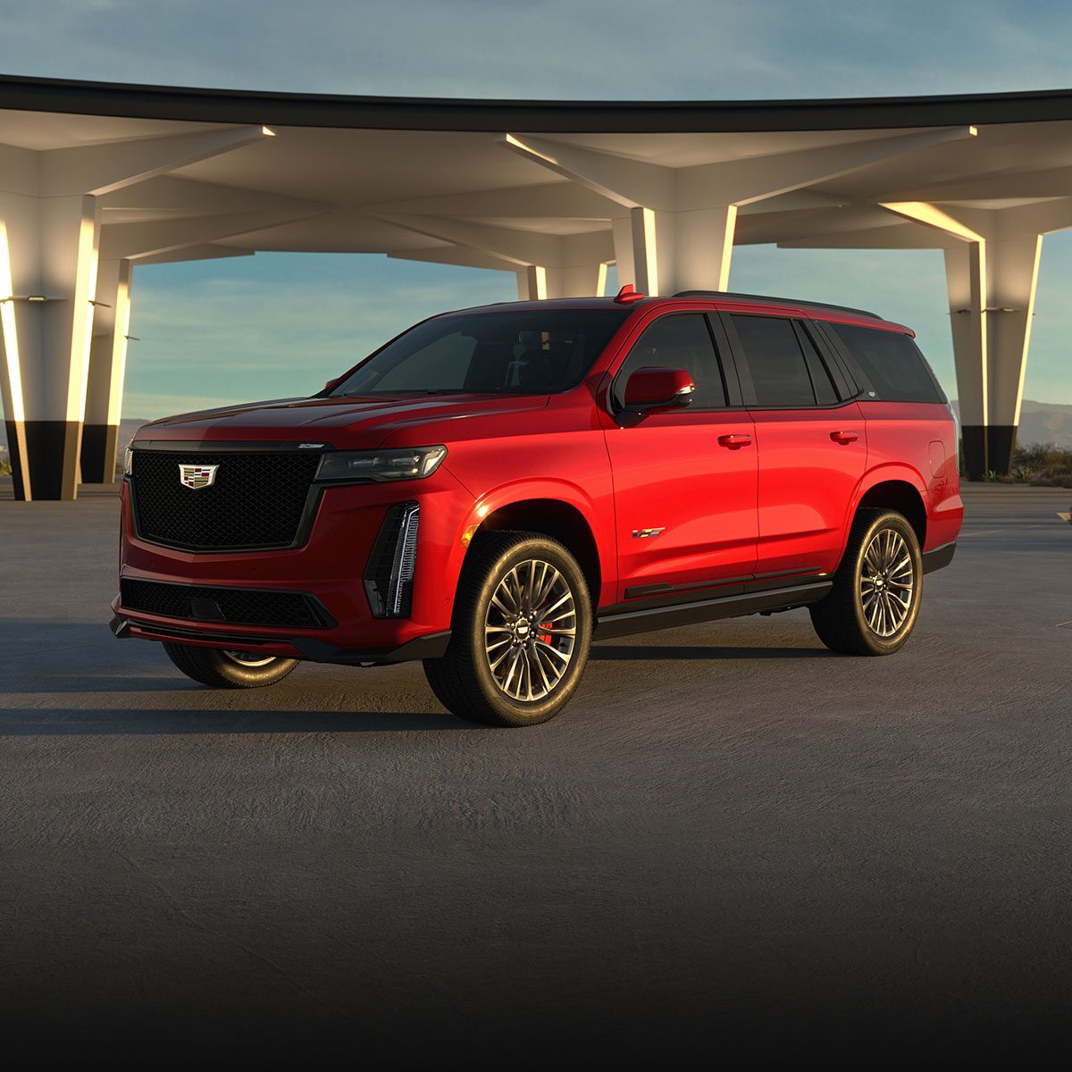 Vista de medio perfil de una Cadillac Escalade-V 2025 roja estacionada bajo un paso elevado